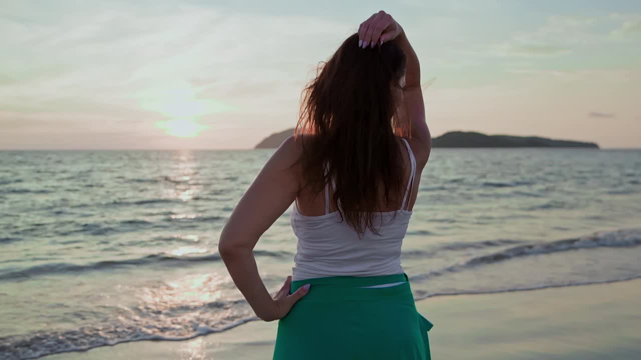 夏日夕阳下，年轻女子在沙滩上欣赏海景视频素材