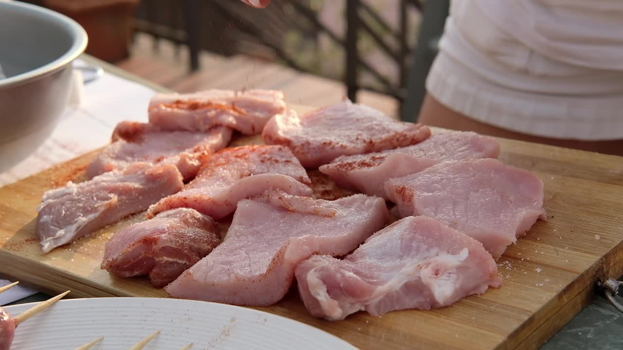 一个女人的手加香料腌盐和橄榄油与新鲜迷迭香牛排烹饪在家庭露台烧烤视频下载