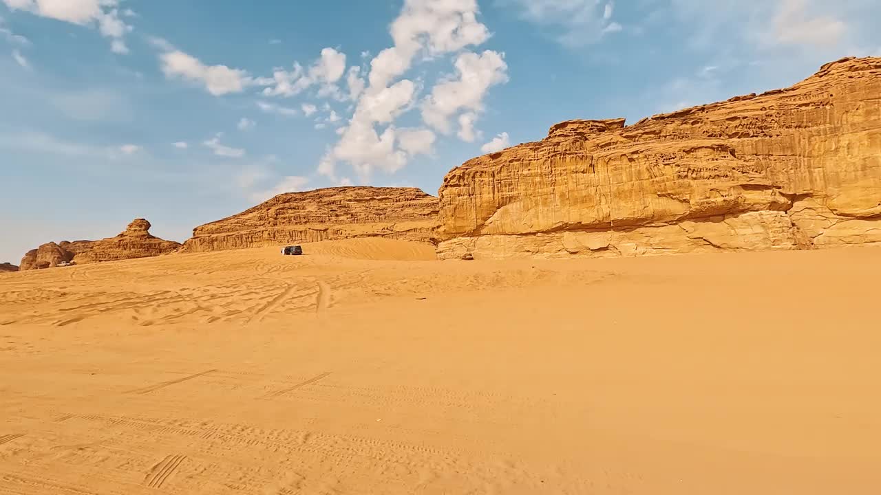 在沙特阿拉伯阿卢拉典型的沙漠景观中行驶，沙地上有一些山脉，小型车辆和远处的当地人视频下载