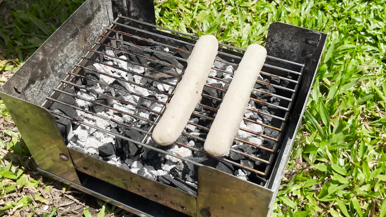 用厨房钳子把香肠放在烤架上的手的特写。户外烹饪概念。烹饪烧烤4K分辨率视频视频素材