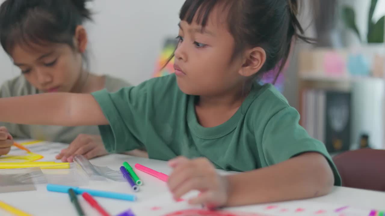 两个小女孩坐在桌子旁，用蜡笔画画。视频下载