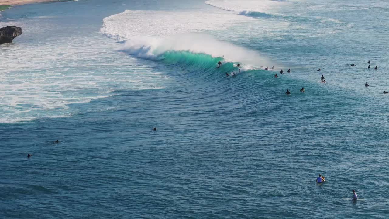 在海浪上冲浪的无人机视图。在巴东巴东海滩和冲浪者一起享受完美的海浪视频素材