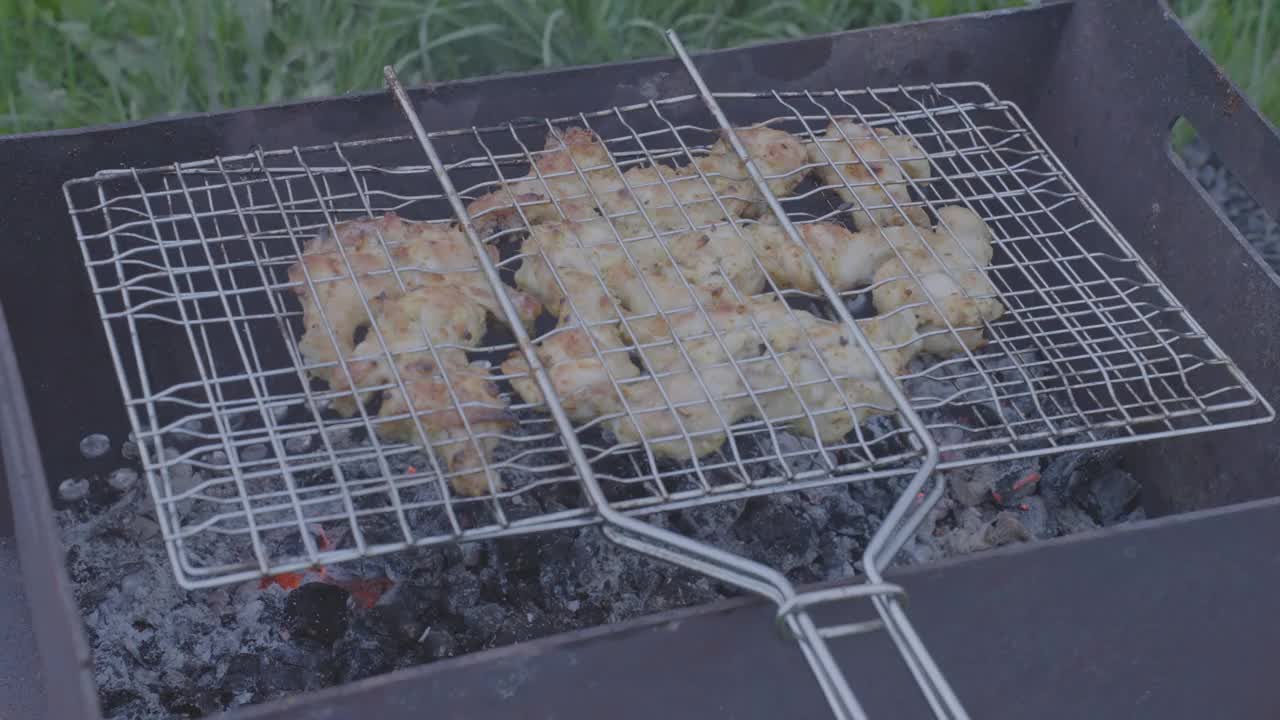 鸡块正在金属烤架上的热煤上烤着。部分煮熟的肉显示褐变的迹象，而下面的余烬发出稳定的热量创造完美的户外烹饪设置视频下载