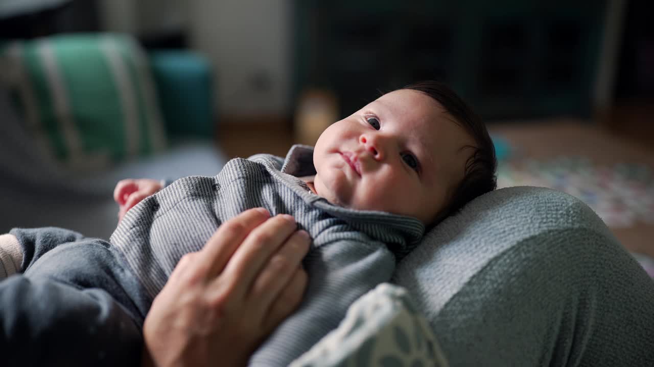 母亲抱着她的孩子，孩子抬起头来，露出满足的表情。柔和的灯光和舒适的环境在客厅里营造出温暖和滋养的氛围视频素材