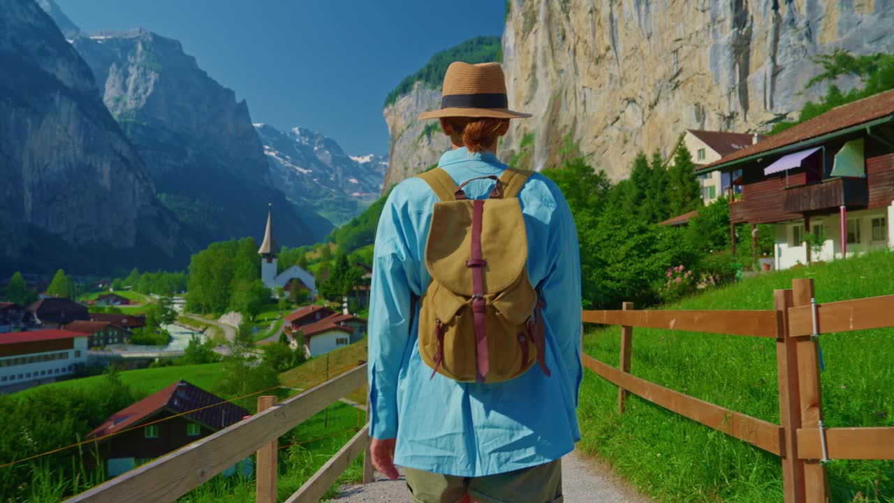 Lauterbrunnen,瑞士。一位年轻的游客背着背包，漫步在阿尔卑斯山上一个有瀑布的著名瑞士村庄的美景中视频素材