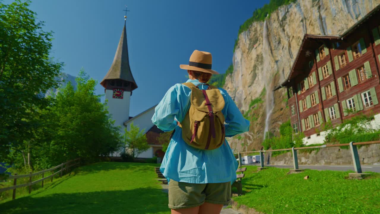 Lauterbrunnen,瑞士。一位年轻的游客背着背包，漫步在阿尔卑斯山上一个有瀑布的著名瑞士村庄的美景中视频素材