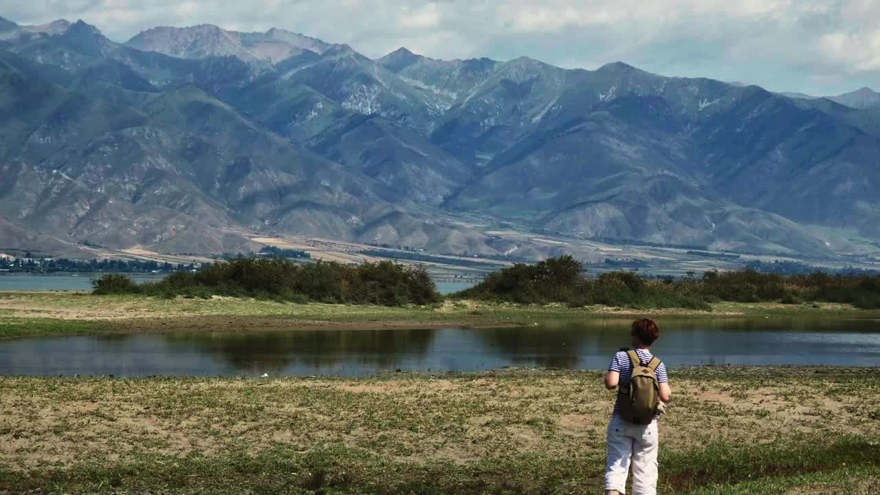 成熟的女游客走在山间的湖岸上视频下载