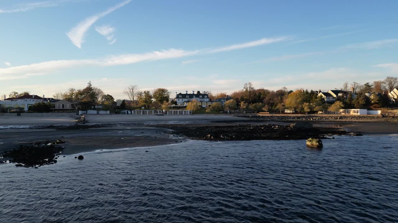 宁静的海滩景色与迷人的房子在背景。天空湛蓝，水面平静，反映出宁静的气氛。非常适合描绘放松和沿海生活视频下载