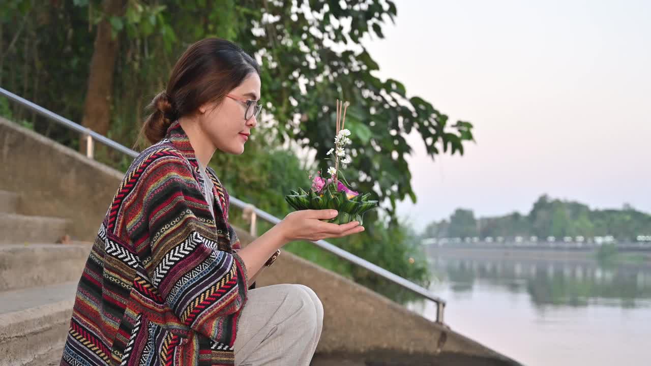 年轻的亚洲妇女拿着水龙包，在泰国的水龙包节上向水女神祈祷，然后把它放在水上。视频下载