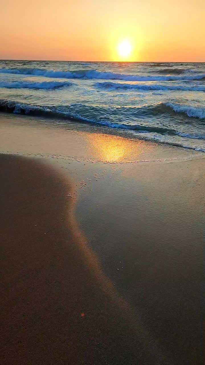 波涛汹涌的海面。在日落黎明的背景下，海浪上有白色的泡沫。蓝色的大海，橘红色的天空，太阳。海岸海岸海岸海岸线。自然背景自然背景风暴慢动作垂直视频下载