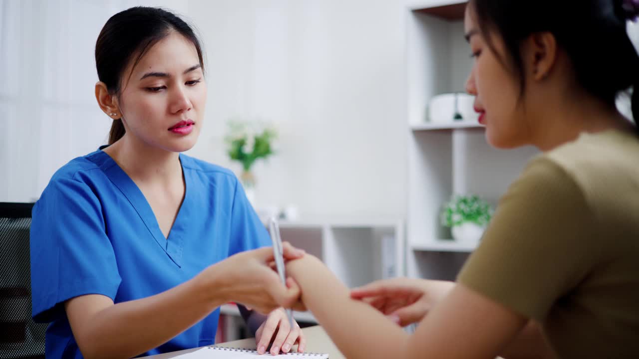 在检查室，穿着手术服的亚洲女医务人员正在检查病人的手腕。视频下载