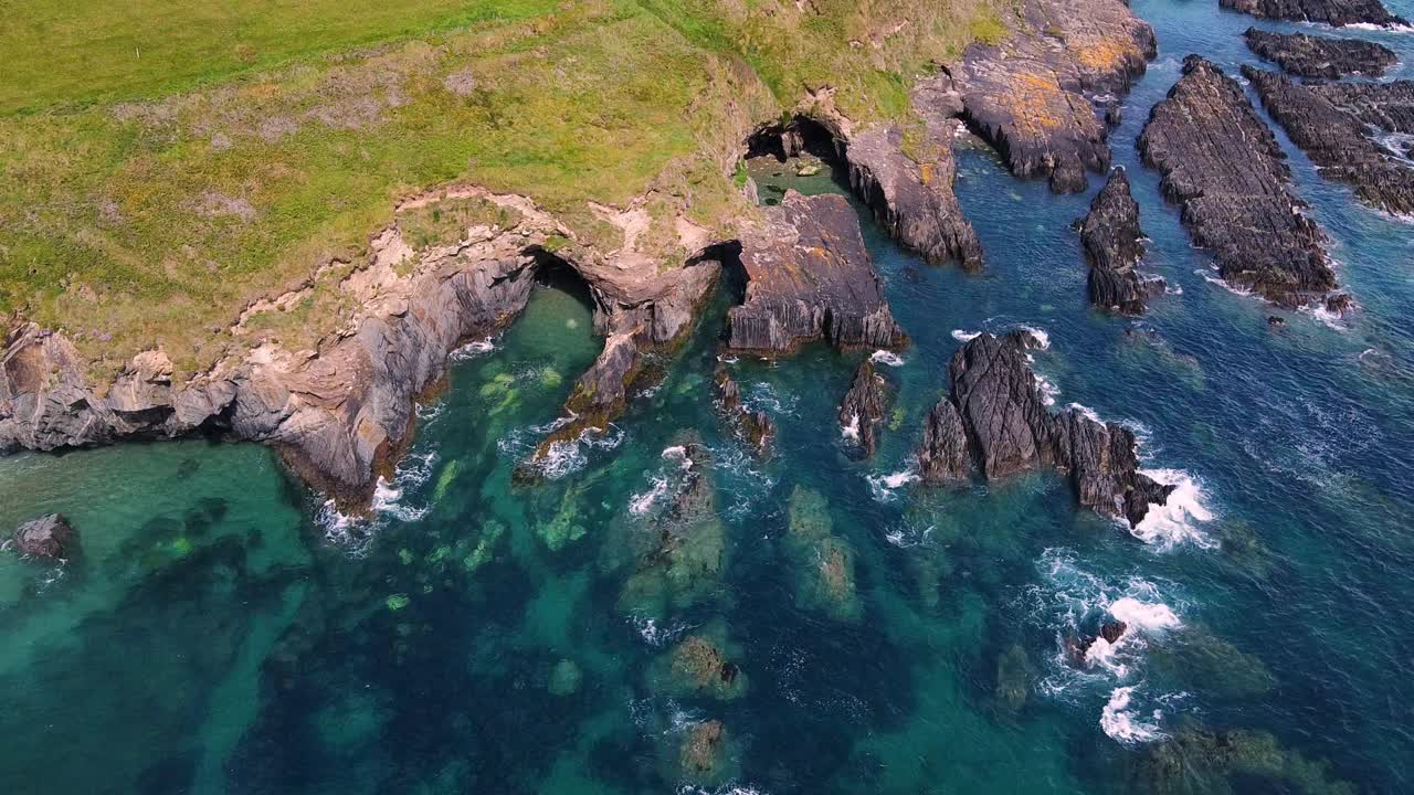 鸟瞰图，岩石海岸线和清澈的蓝色海水。岩石是深灰色的，有些部分被淹没了。视频素材