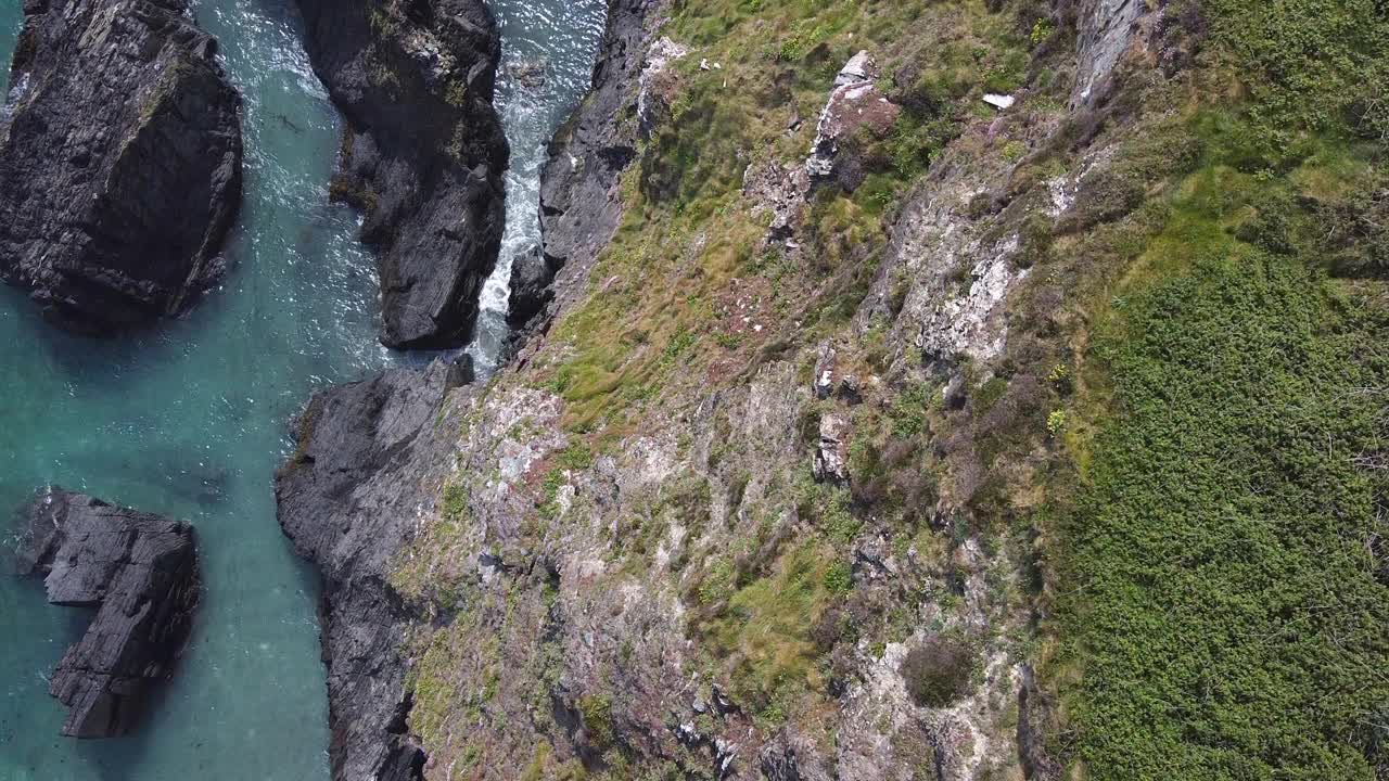 这段视频从鸟瞰多岩石的海岸线。深灰色的岩石与蓝绿色的海水交汇，在那里可以看到白色的浪花。视频素材