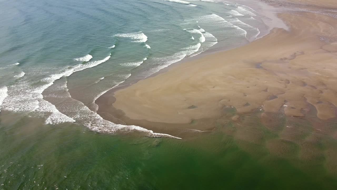 低潮时海浪冲刷沙滩海岸线的鸟瞰图。视频素材