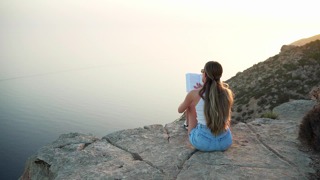 夕阳西下，一个女人正在看书，欣赏着美丽的景色视频下载