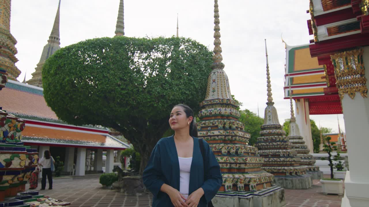 在一个晴朗的日子里，一名妇女站在泰国一座历史悠久的寺庙里，站在华丽的宝塔之间，欣赏着丰富的文化遗产。视频下载