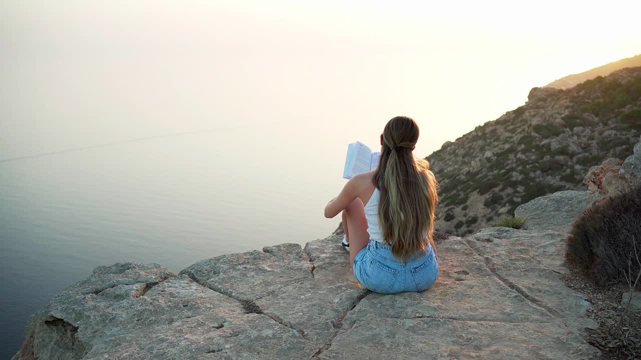 夕阳西下，一个女人正在看书，欣赏着美丽的景色视频素材