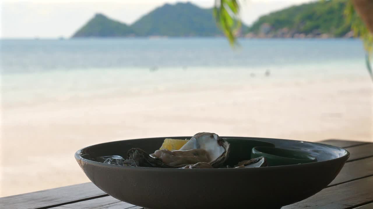 木桌上的海鲜拼盘俯瞰着宁静的海滩和岛屿视频素材