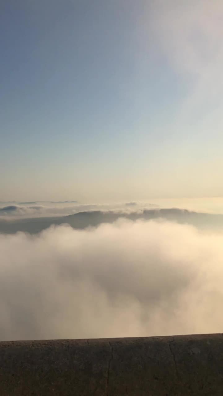 一段视频捕捉了从山顶到隐藏在云层下的山谷的垂直扫描。视频下载