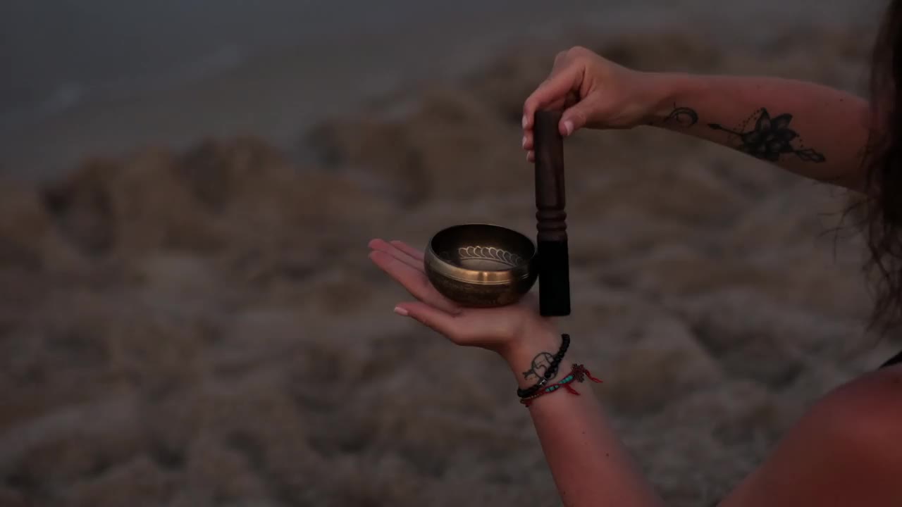 夏日的傍晚，年轻美丽的女孩在海边的沙滩上冥想并演奏着碗歌视频下载