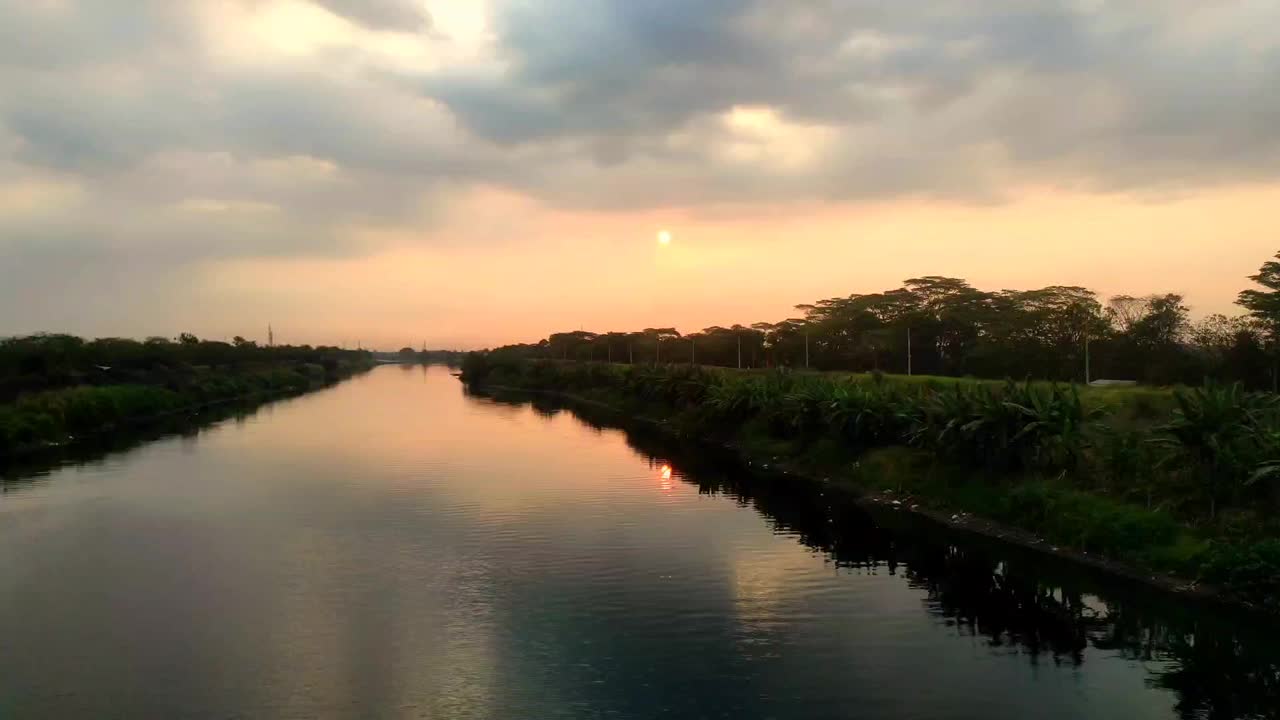 在多云的夕阳下，大河被树木和灌木包围着视频下载