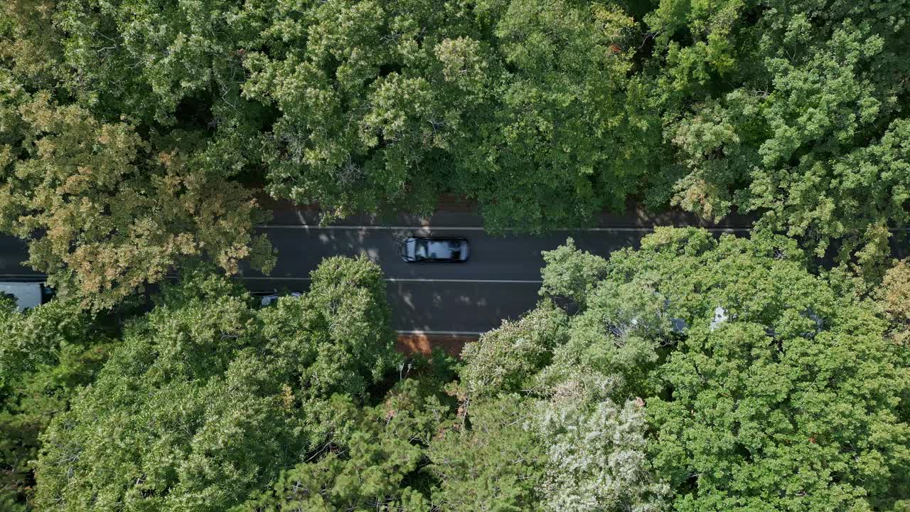 无人机拍摄的一段视频显示，一辆汽车行驶在蜿蜒的道路上，穿过郁郁葱葱的绿色森林。俯视图突出了人造道路与自然环境之间的对比视频素材