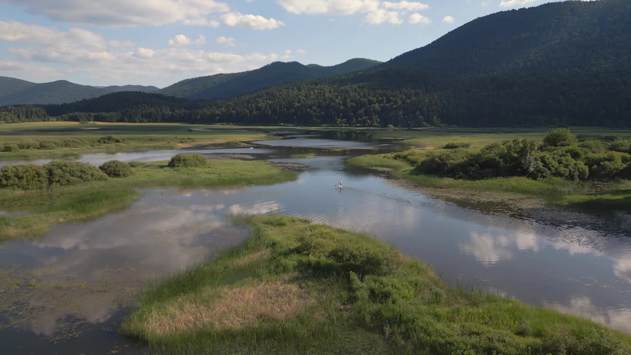 山湖风景和一个站立板手在平静的水面上划桨视频下载