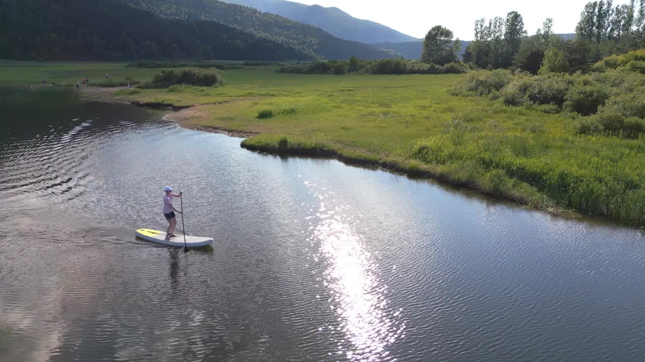 女子划着站立式桨板，探索湖岸，享受大自然视频素材