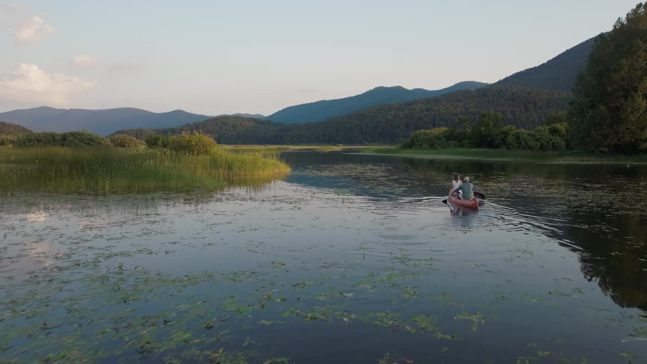 一对夫妇乘独木舟穿越山间湖泊，享受夏日的自然风光视频素材