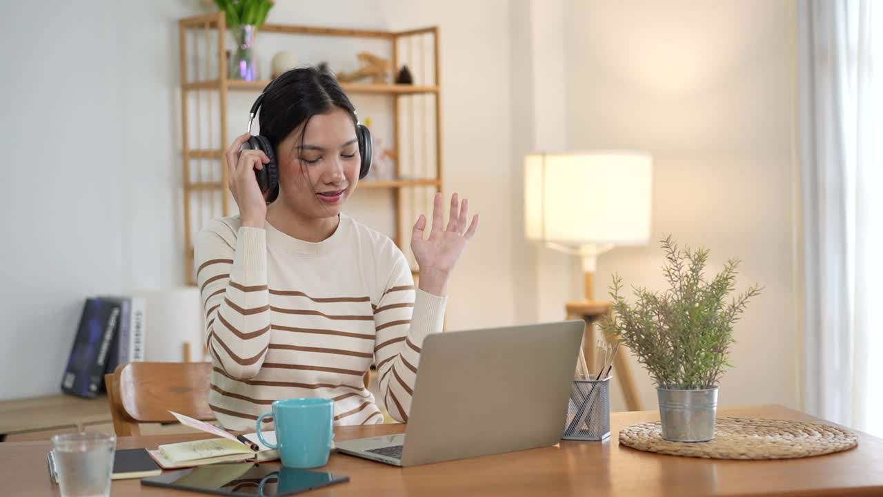 快乐的年轻美丽的亚洲女人微笑着在家里的厨房桌子上使用笔记本电脑。年轻的成年亚洲人在家里用现代便携式电脑远程工作。视频下载