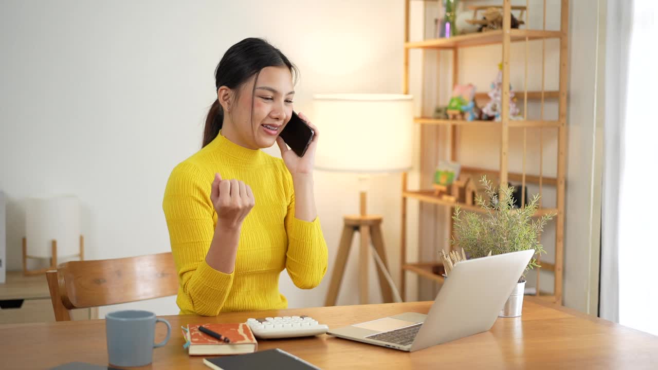 亚洲女性一边在家里用笔记本电脑工作，一边打电话。视频下载