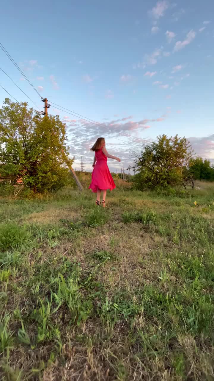 夕阳下，一个快乐的女人在乡间的田野里穿着粉红色的衣服纺纱视频下载