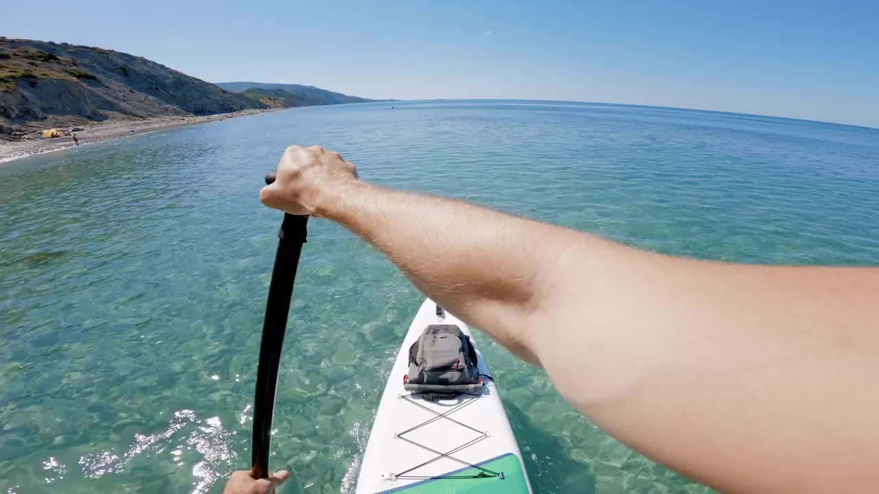 男子在透明的海面上划船。夏季站立桨板的第一人称视角。视频素材