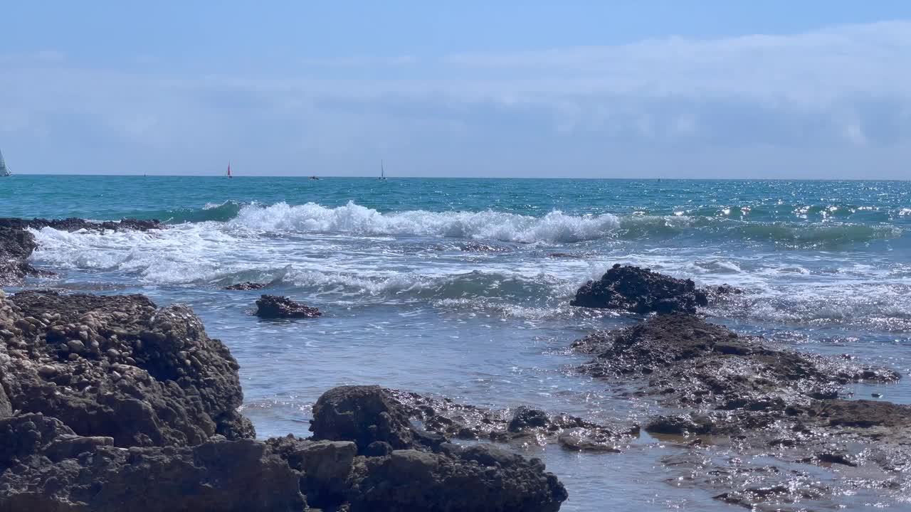 海浪冲击着海滩上的岩石，海浪在空气中飞溅，阳光反射在水面上。自然的海浪运动，在傍晚撞击着粗糙的石头海岸。自然风光为宁静、旅行、氛围。视频下载