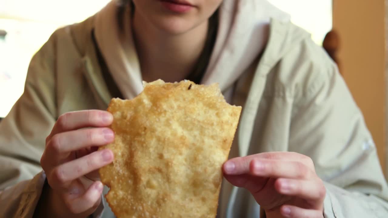 一个小女孩坐在咖啡馆里的桌子旁吃着炸干酪派。视频下载