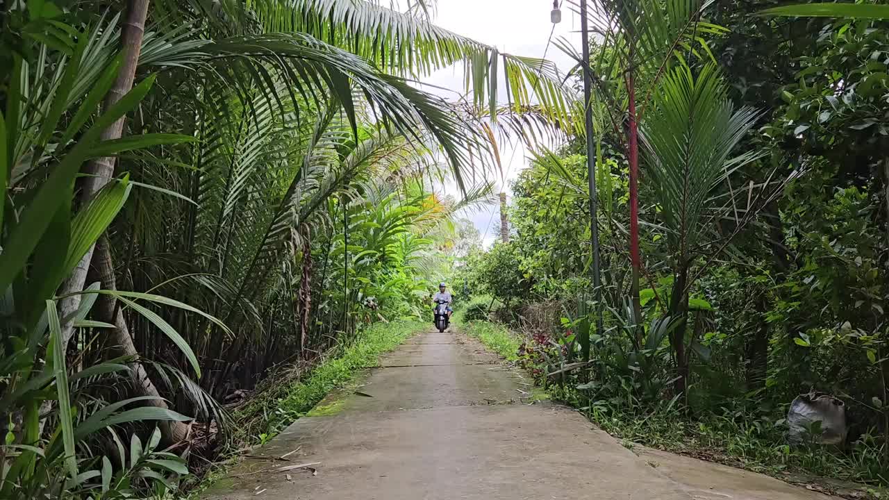 上午，在越南湄公河三角洲永隆省芒提区村庄狭窄的街道上，一名男子驾驶着摩托车。视频素材