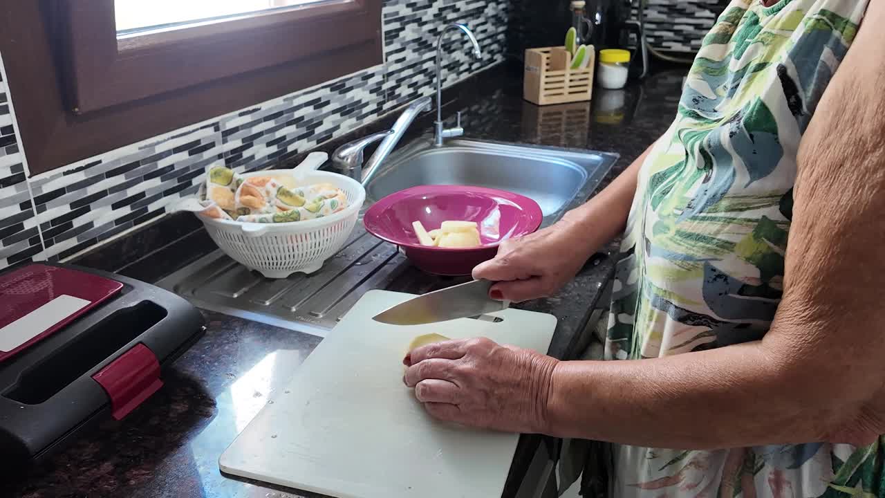 正午时分，一个女人在一个小厨房里用厨刀切土豆的静态特写。视频素材