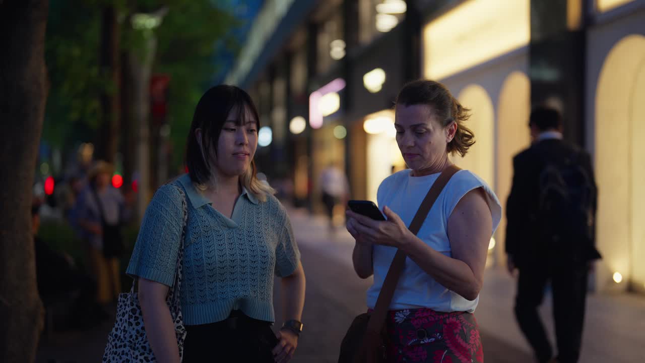 在东京的城市街道上，女性独自旅行者使用人工智能手机应用程序与当地人交流并问路视频素材