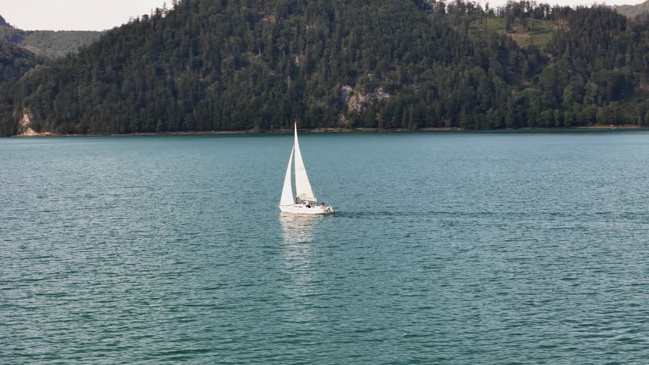 帆船在平静的碧绿湖水上滑行，背景是郁郁葱葱的山丘视频素材