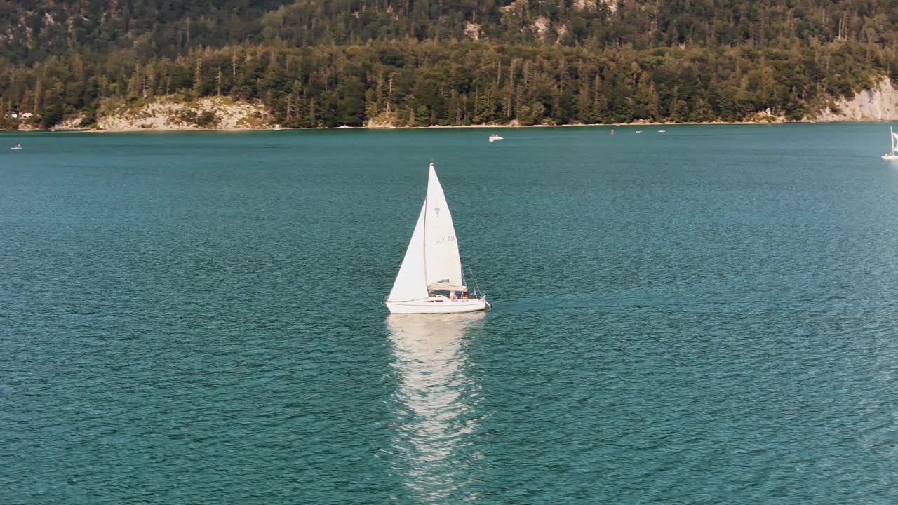 帆船在平静的绿松石湖上滑行，背景是森林覆盖的海岸视频素材