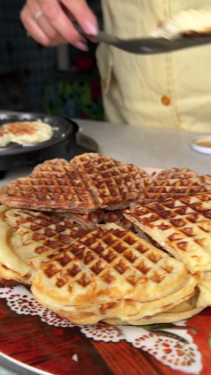 一位女士从电动华夫饼机中取出准备好的华夫饼。旁边是准备好的华夫饼。垂直视频。视频下载