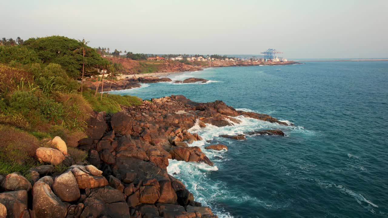 鸟瞰碧绿的海浪撞击岩石海岸线，大海在布满巨石的海岸线周围编织。Kovalam海滩，印度喀拉拉邦。视频下载