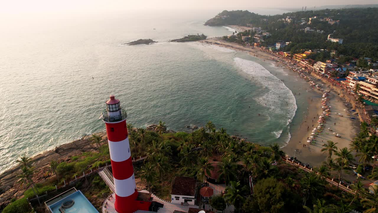 日落时海上海岸线上的灯塔，鸟瞰图。印度喀拉拉邦的Kovalam海滩和灯塔。视频下载