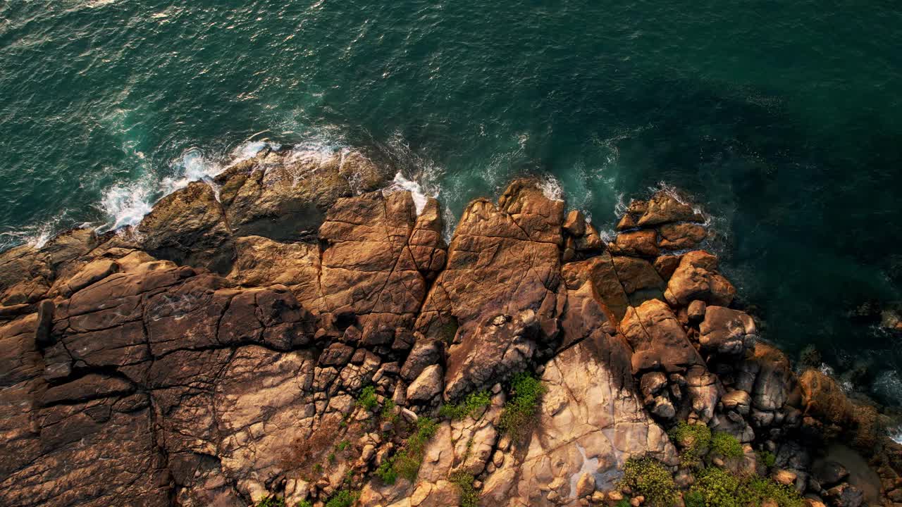 鸟瞰碧绿的海浪撞击岩石海岸线，喜怒无常的大海在布满巨石的海岸线周围编织视频下载