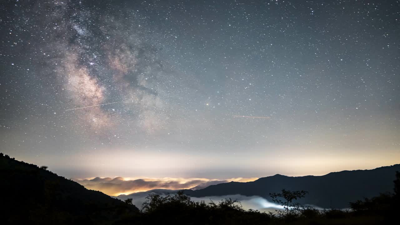 在宁静的夜空中，星星在银河下的薄雾山脉上闪烁视频素材