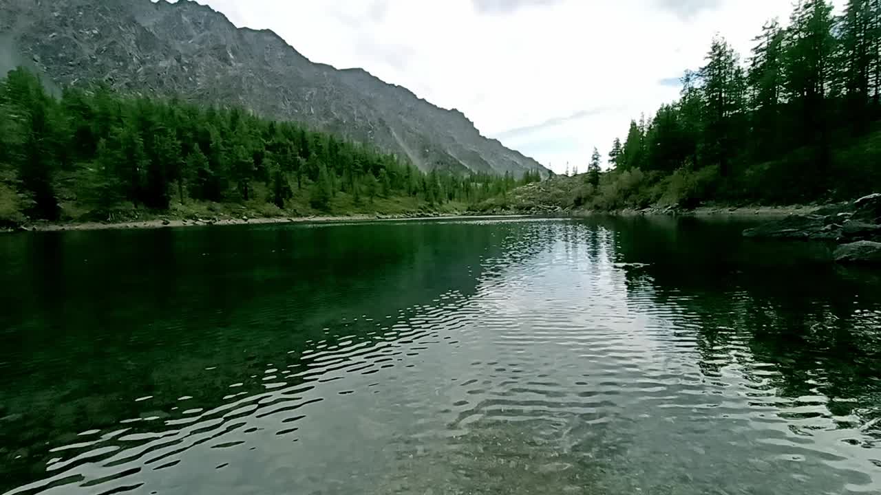 在一个阳光明媚的夏日，一个美丽的湖泊表面上的涟漪，绿松石般的水夹在高山的斜坡之间。视频下载