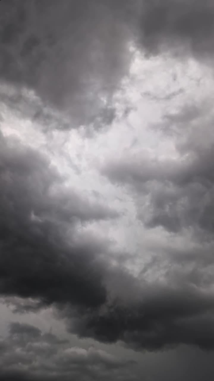 灰色的雷雨云飘过天空，偶尔被闪电照亮，预示着暴风雨、下雨和打雷。垂直视频。视频素材