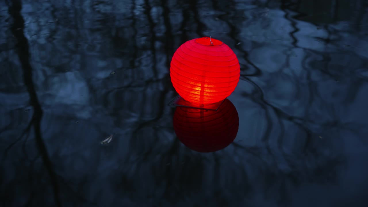 手持拍摄的红纸灯笼在节日期间漂浮在河水上视频下载