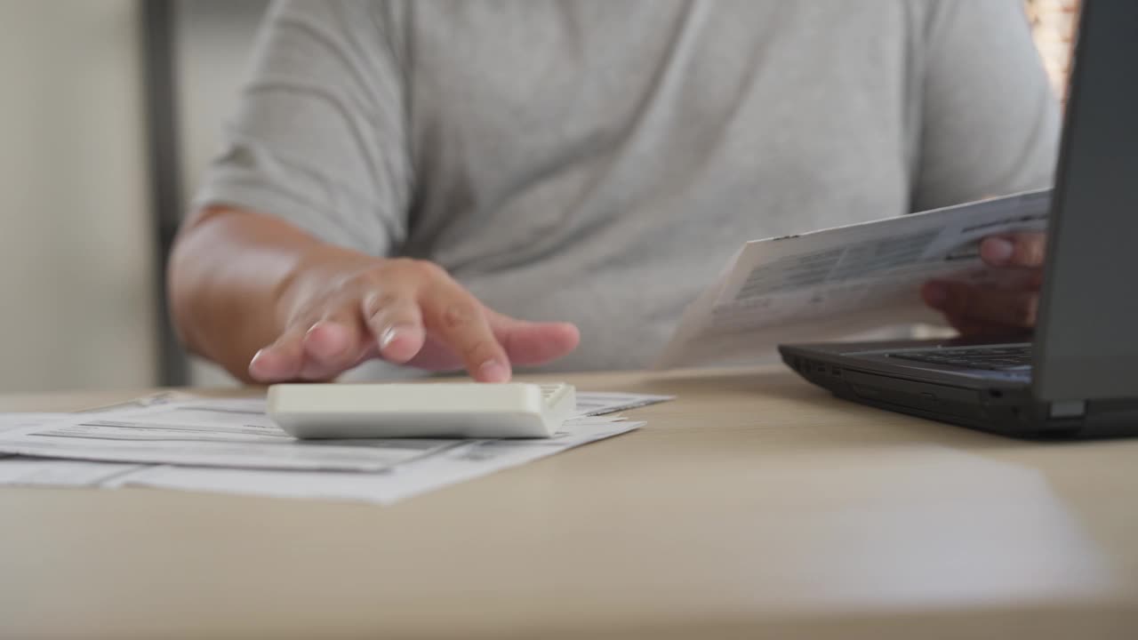 一个男人用计算器计算家里的财务账单，用笔记本电脑计算费用的特写视频素材