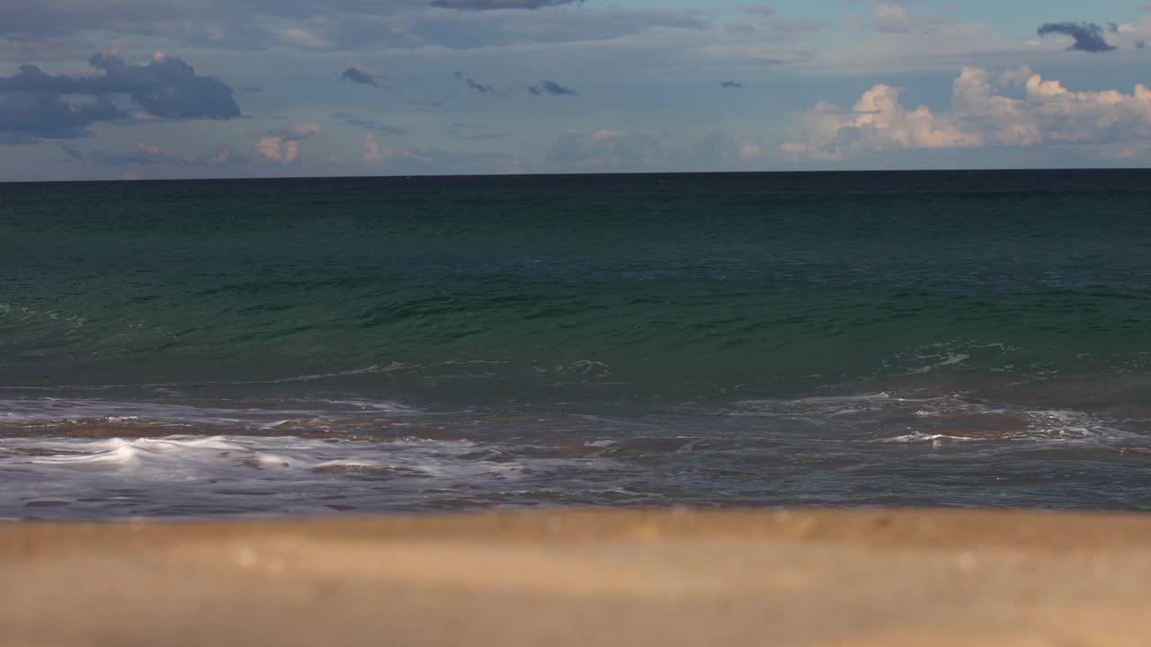 在美丽的金色午后阳光下，五彩缤纷的海岸波浪沿着海滩卷曲和破碎。视频下载